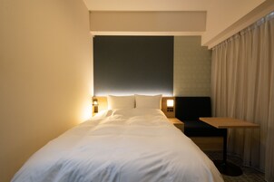 A hotel room with a large bed, a bedside table, a chair, and a small table.