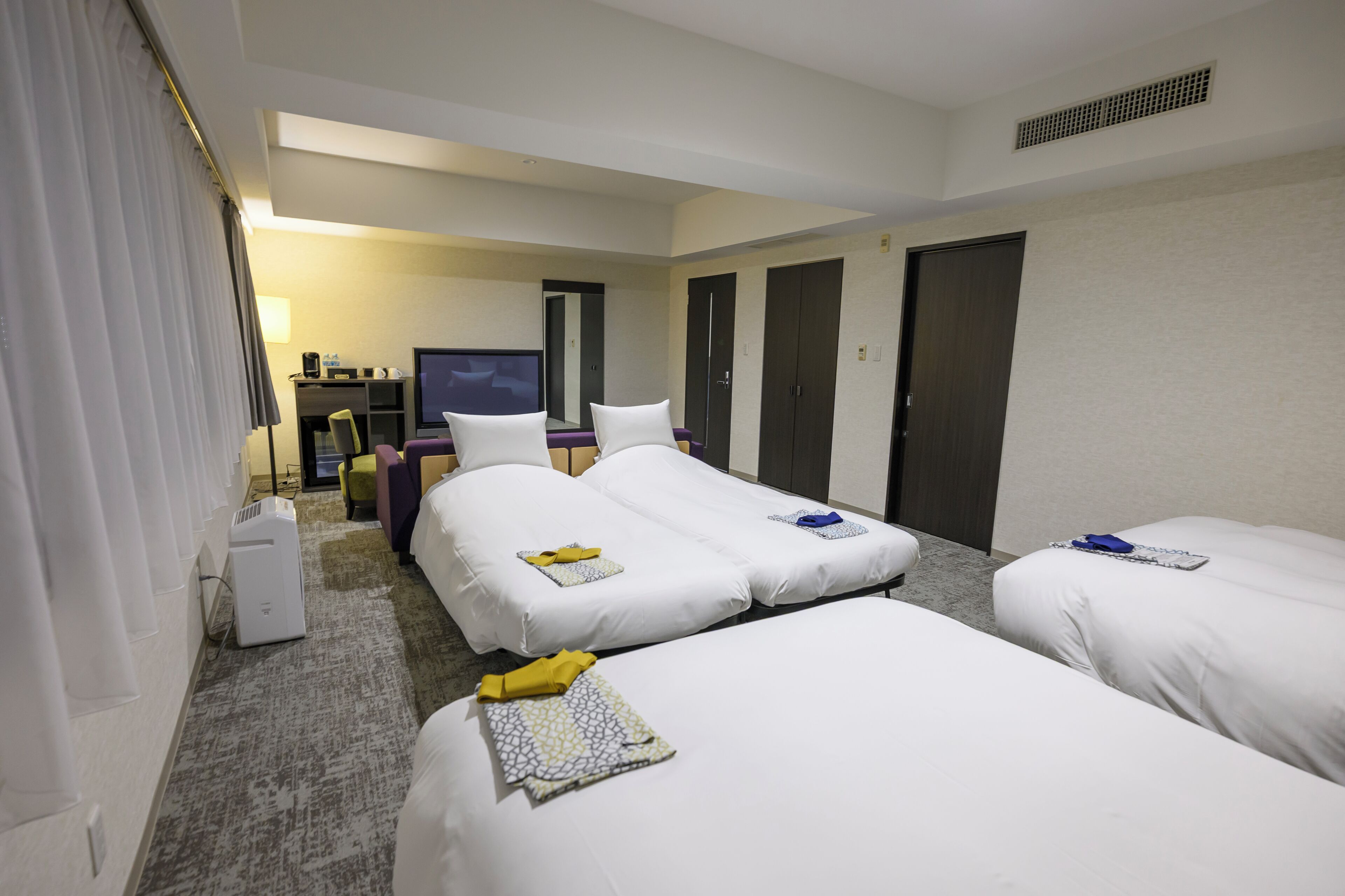 A hotel room with two single beds, a desk with a computer, a TV, and a wardrobe.