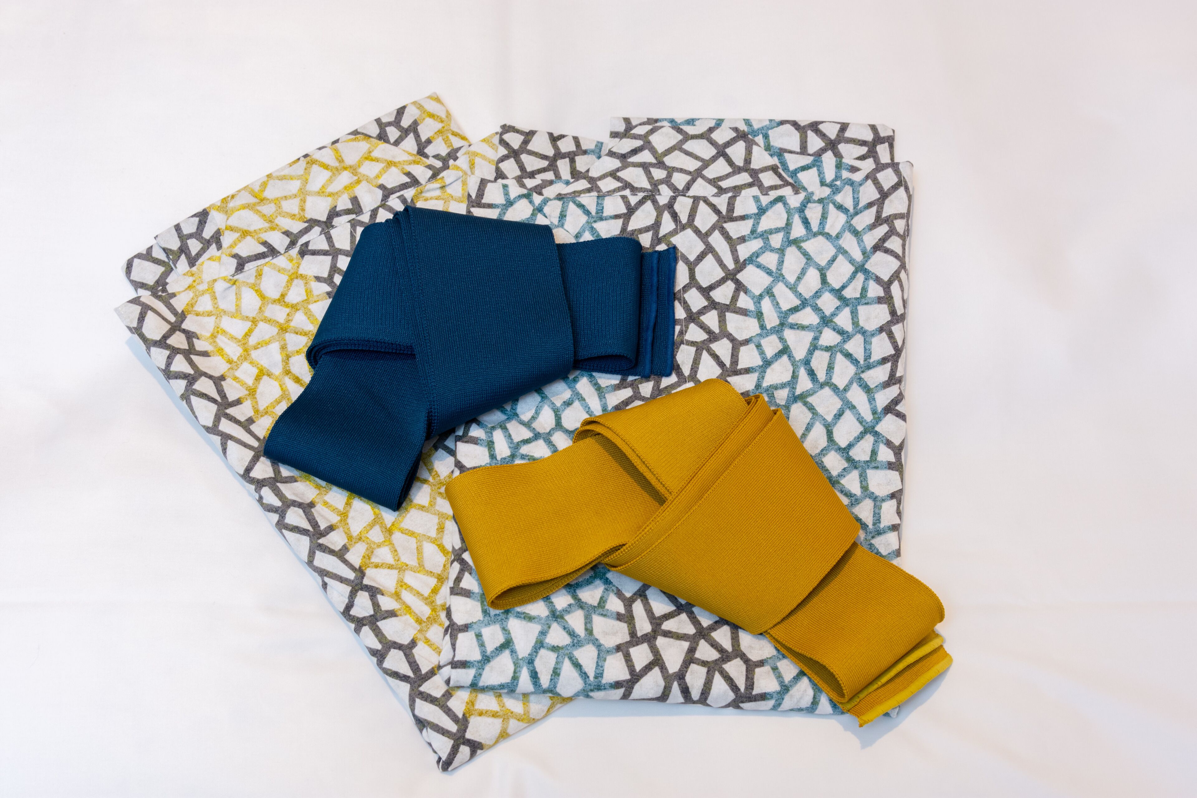A bed with a patterned bedspread and two folded pieces of clothing on it.
