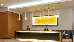 A reception desk with two staff members, a large abstract artwork on the wall, and modern pendant lighting.
