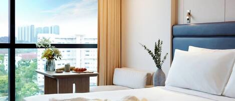 Habitación de hotel con una cama grande, una mesita de noche con un jarrón de flores y vistas a la ciudad a través de la ventana.