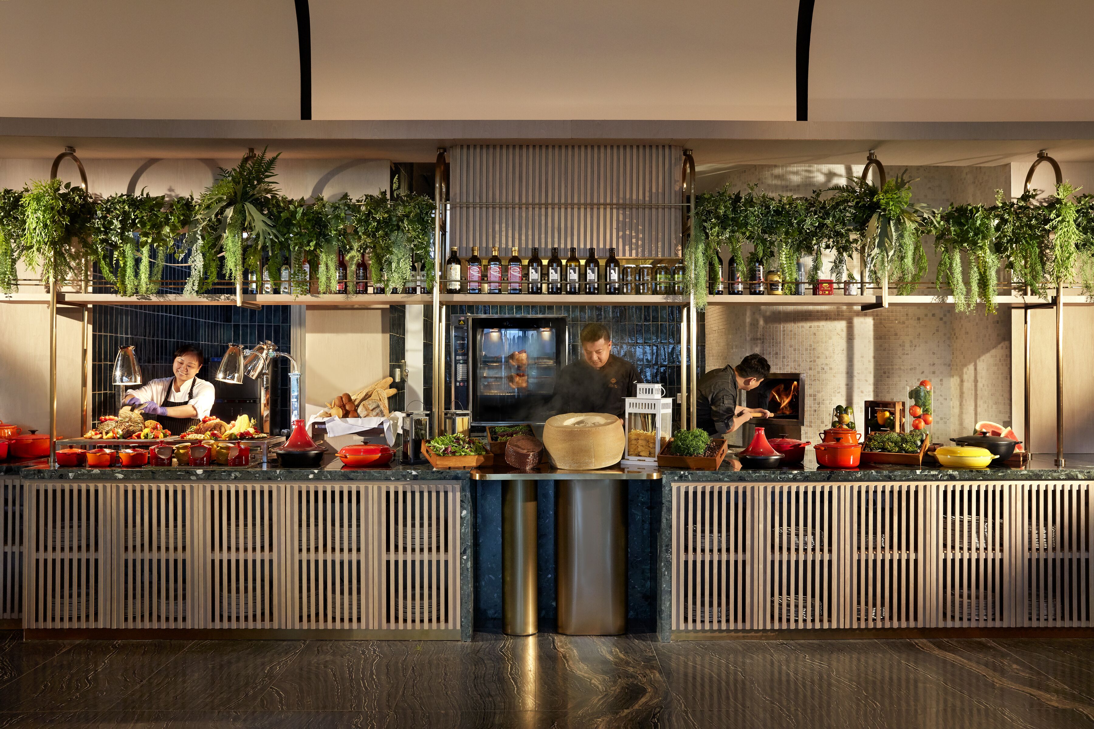 A modern kitchen with a central island, various cooking utensils, and hanging plants.