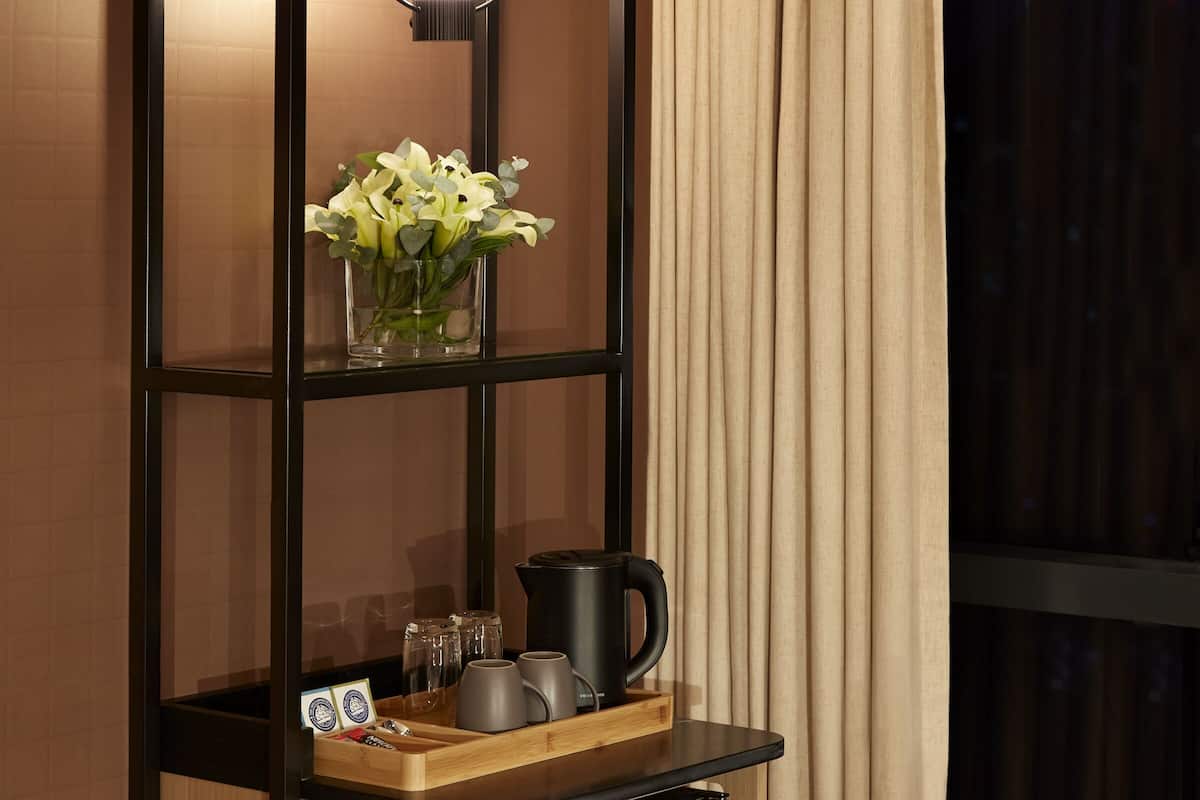 A modern room with a wooden cabinet, a glass vase with flowers, a coffee maker, and a hanging light fixture.