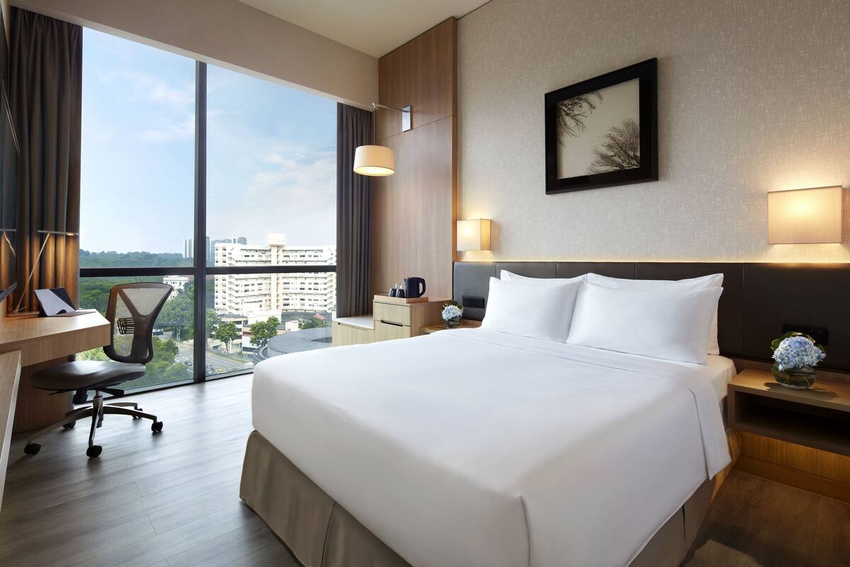 A hotel room with a large bed, a desk, a chair, and a view of the city.