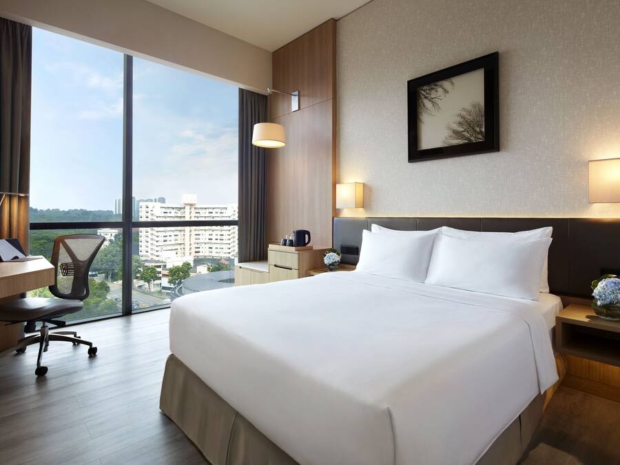 A hotel room with a large bed, a desk, a chair, and a view of the city.