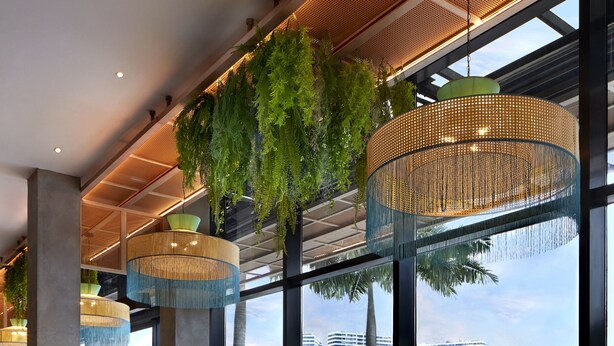 Un amplio comedor interior con techos altos, ventanas grandes y plantas colgantes.
