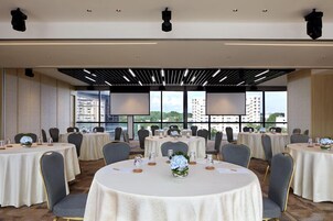 A conference room with round tables, chairs, and a city view through large windows.