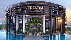 Un moderno bar-restaurante junto a la piscina llamado Verandah, con diseño circular, asientos al aire libre y vistas al horizonte de la ciudad.