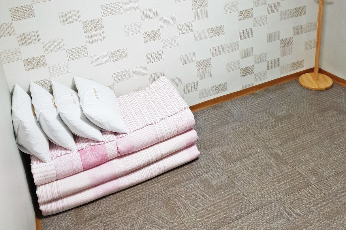 A room with patterned wallpaper, a standing lamp, and neatly folded blankets.