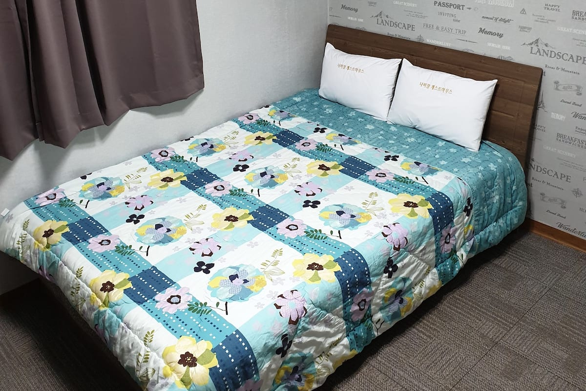 A bed with a floral quilt, a brown curtain, and a wall with various travel-related words.