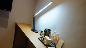 Et skrivebord med en skrivebordslampe, en kaffemaskine, to kopper, en vandflaske og et skilt.