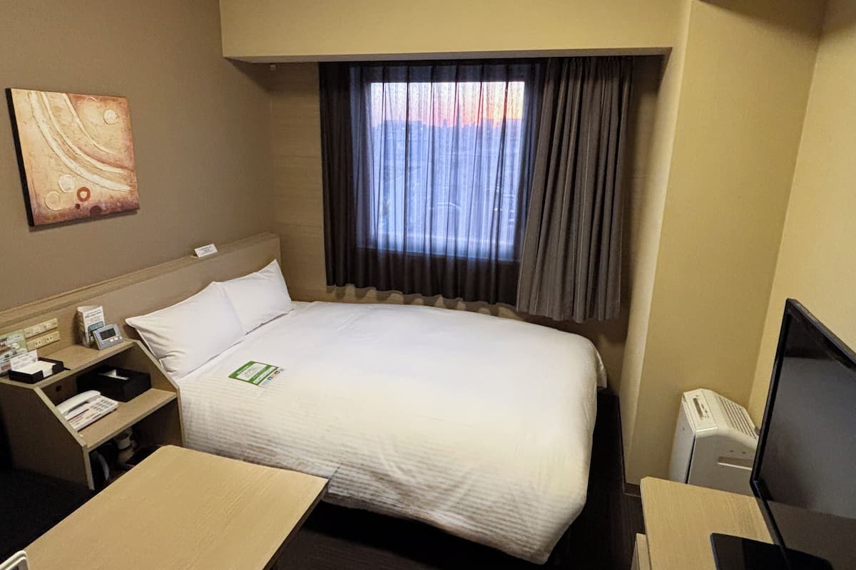 Ein Hotelzimmer mit Bett, Schreibtisch, Fernseher und einem Fenster mit Vorhängen.