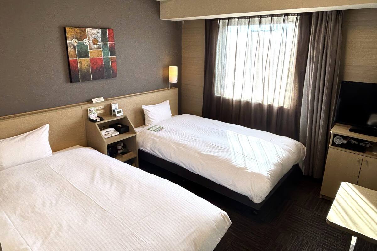 Ein Hotelzimmer mit zwei Betten, einem Fernseher, einem Schreibtisch und einem Bild an der Wand.
