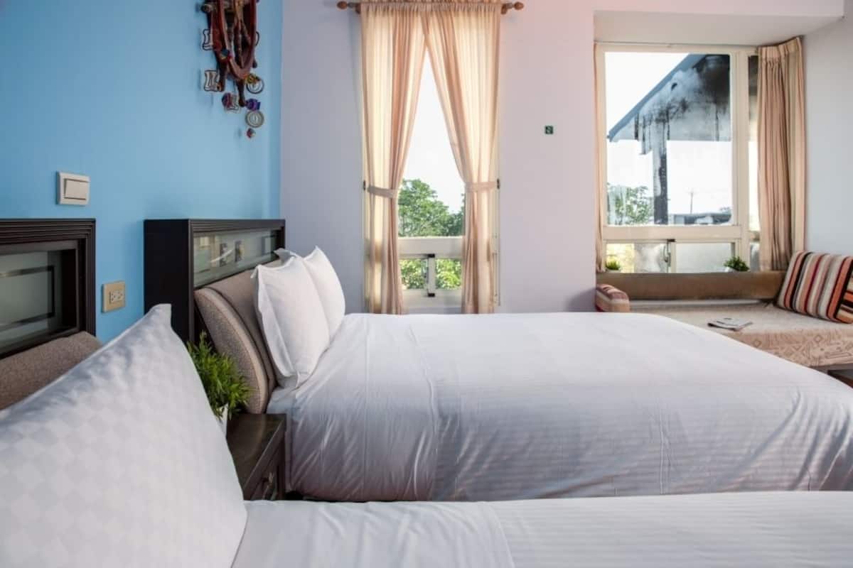A bedroom with two beds, a TV, and a window with curtains.