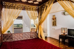 A room with a red bedspread, wooden headboard, and a view of greenery outside. - Vanilla Sky (Wujie)