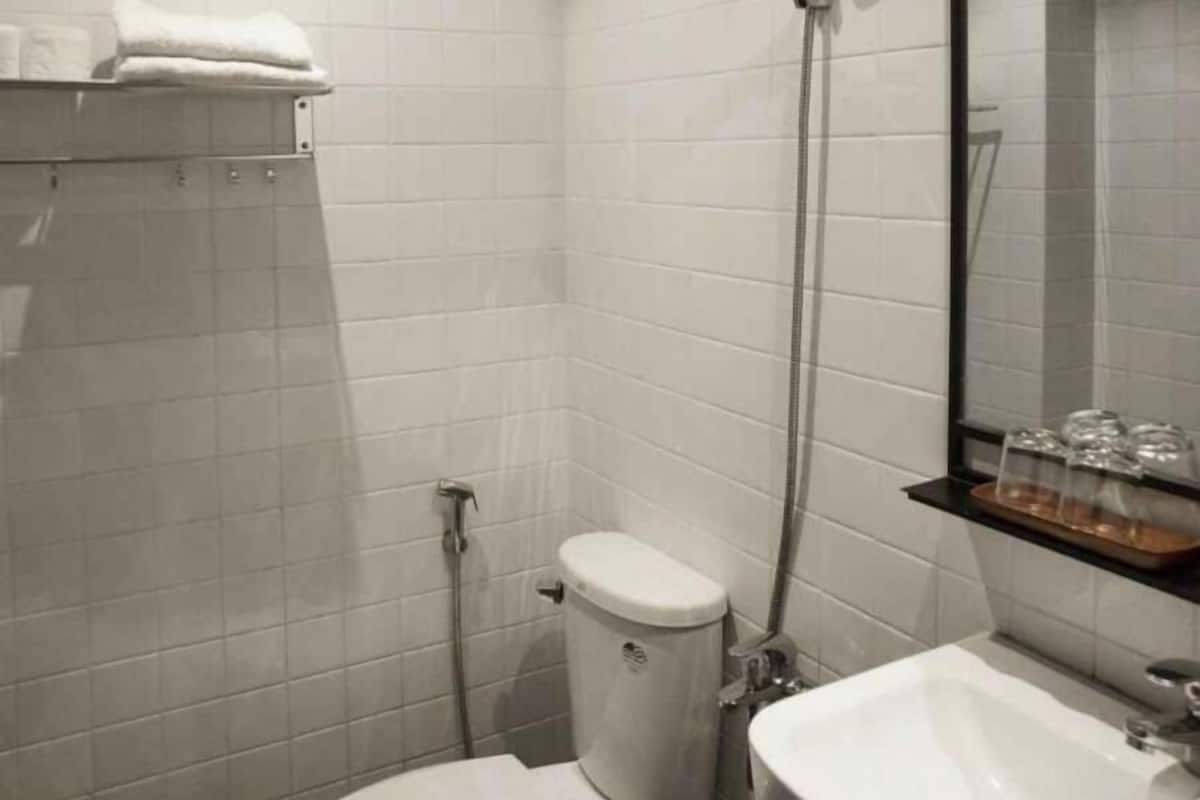 A bathroom with white tiles, a toilet, a shower, a sink, and a mirror.