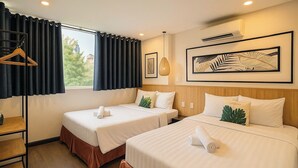Ein Hotelzimmer mit zwei Betten, einem Holzkopfstück, einem Fenster mit Vorhängen, einer Hängeleuchte und einem gerahmten Kunstwerk an der Wand.