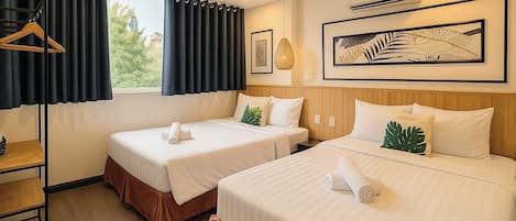 A hotel room with two beds, a wooden headboard, a window with curtains, a hanging light fixture, and a framed artwork on the wall.