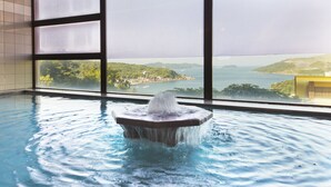 A swimming pool with a water fountain, large windows, and a view of a coastal landscape. - Toba View Hotel Hanashinjyu (Toba)