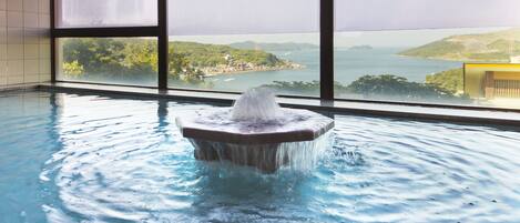 Una piscina con fuente de agua, ventanas amplias y vistas al paisaje costero.