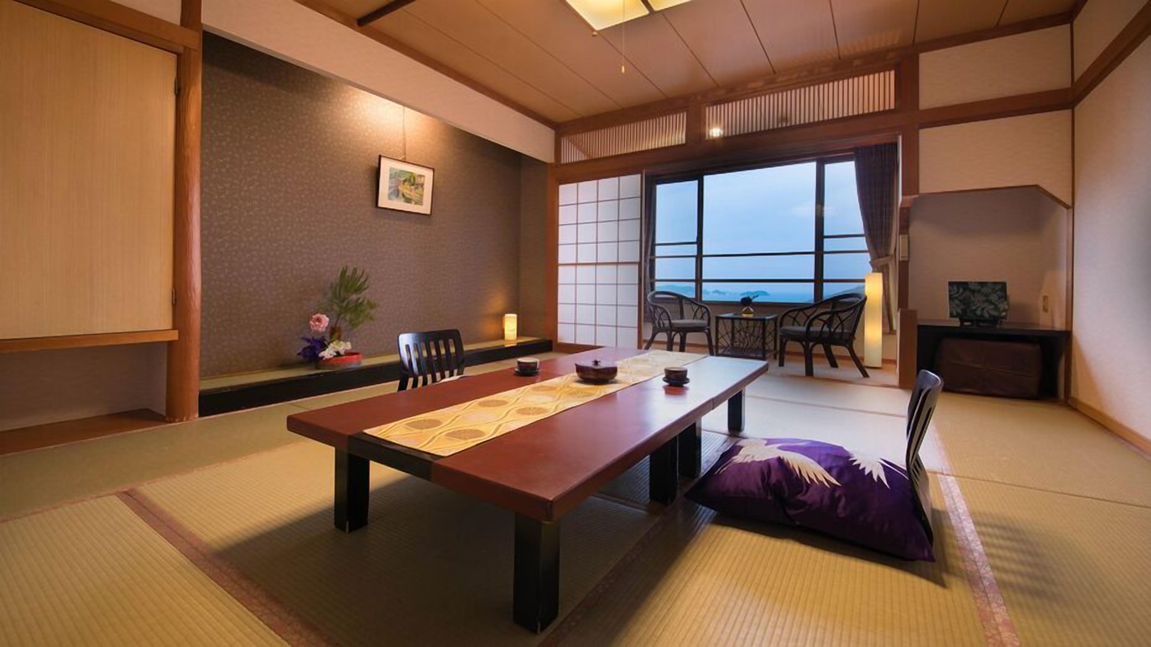 A traditional Japanese-style room with tatami flooring, a low table with a placemat, a low wooden desk, and a view through large windows.