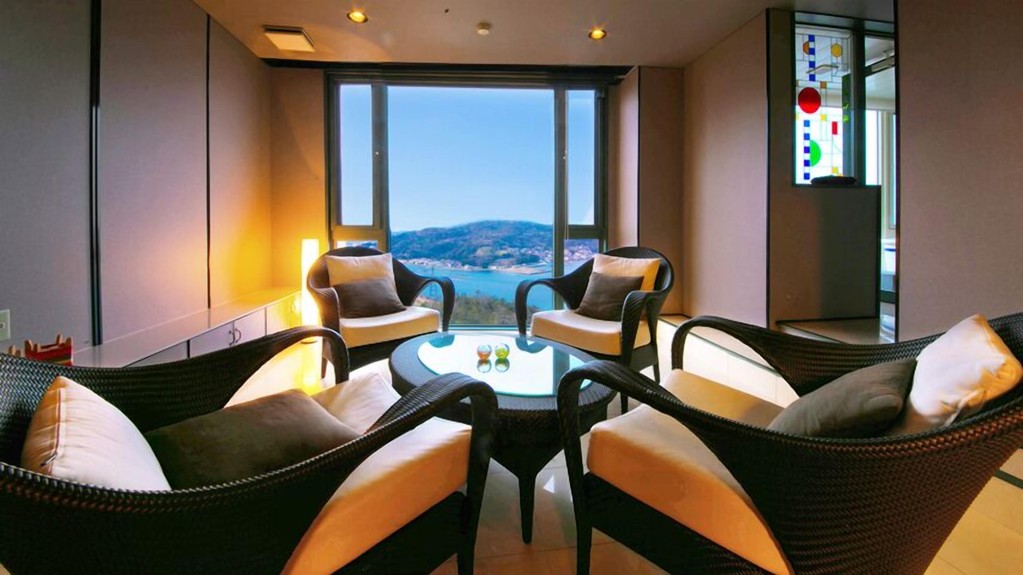 A modern room with wicker furniture, a glass table, and a large window offering a view of the landscape.