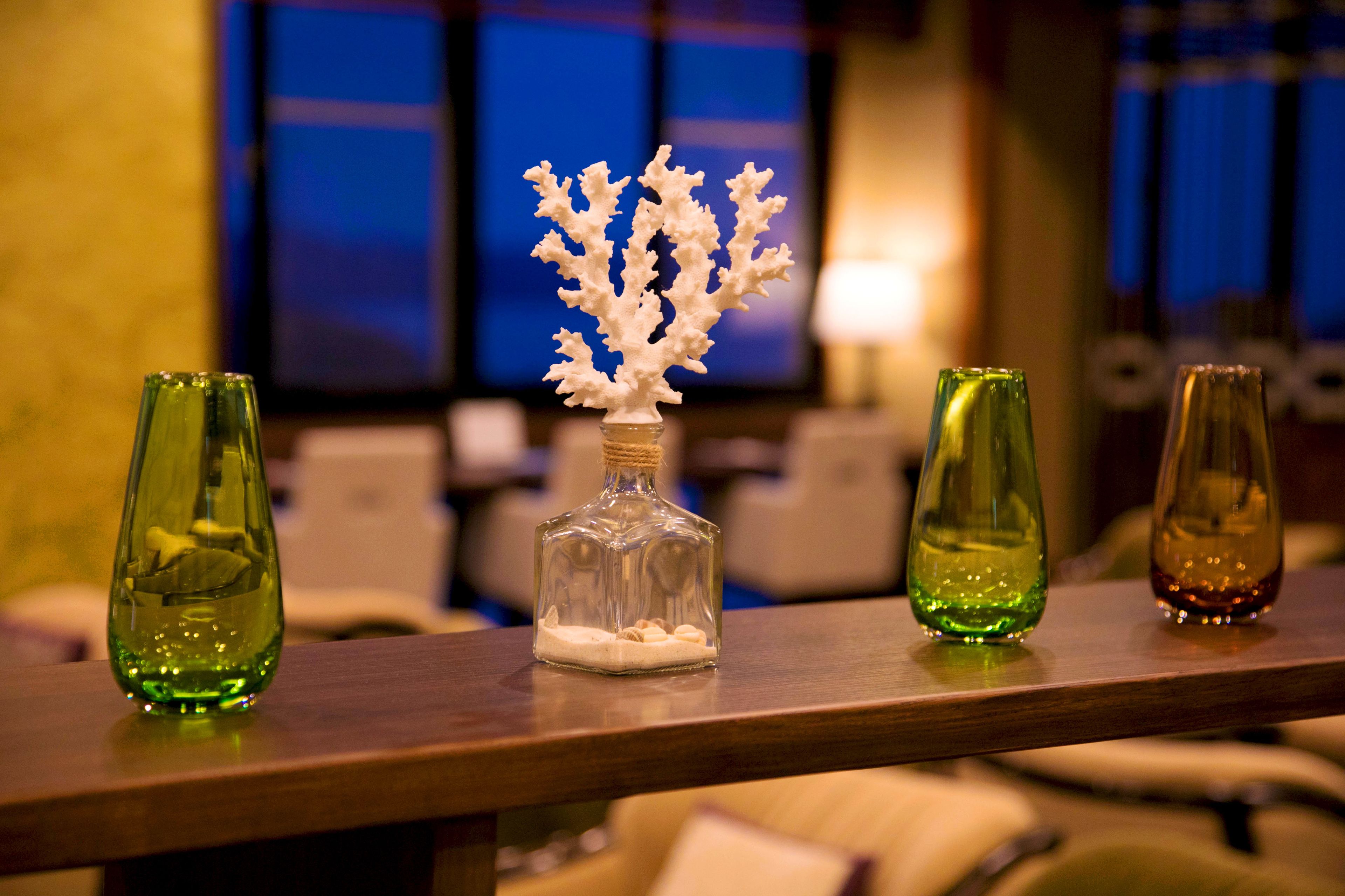 A bar area with three glass bottles on a wooden surface, one containing a white coral-like structure.