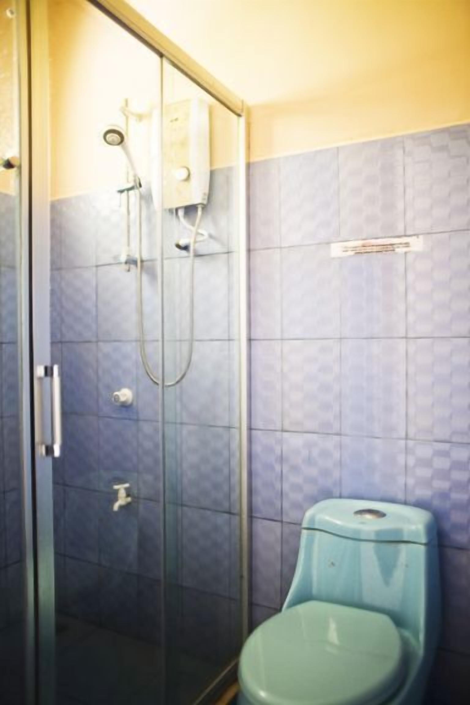 A bathroom with a glass shower enclosure, a blue toilet, and a tiled wall.