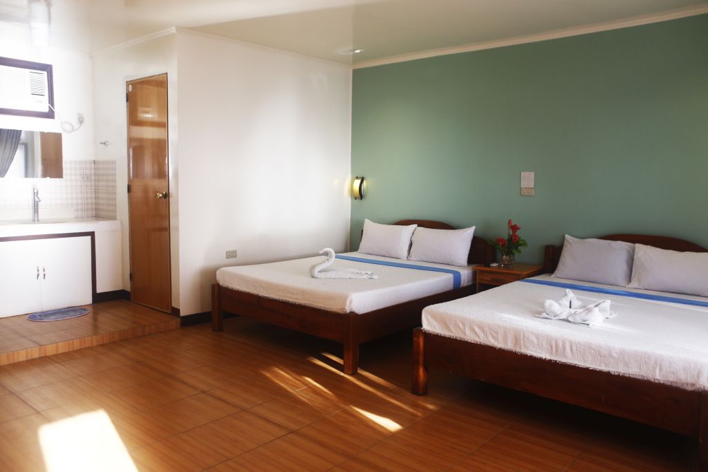 Habitación de hotel con dos camas, suelo de madera, pared verde y un pequeño escritorio con espejo.