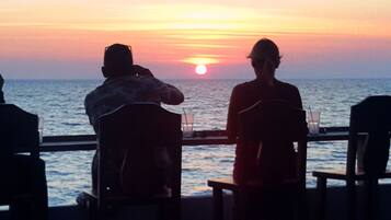 A sunset view from a balcony with two people seated facing the ocean.