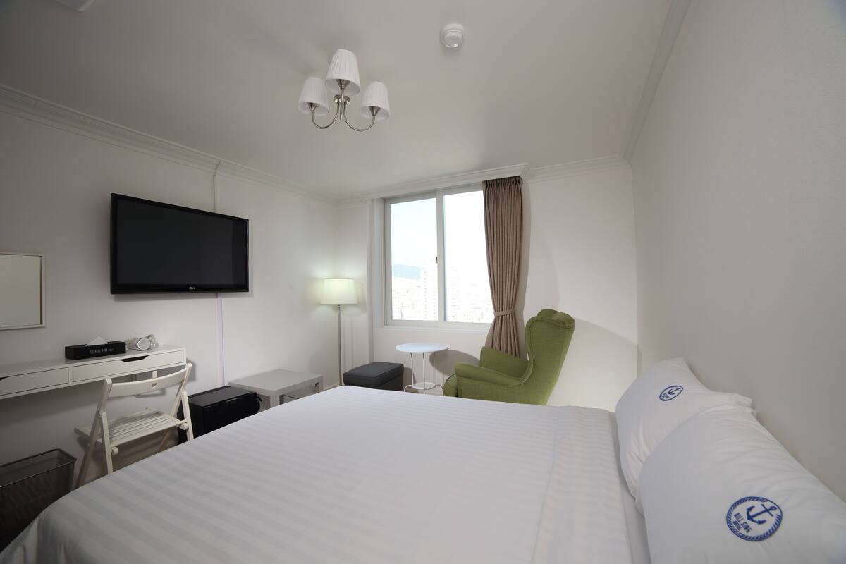 Ein Hotelzimmer mit Bett, Schreibtisch, Stuhl, Fernseher und einem Fenster mit Vorhängen.