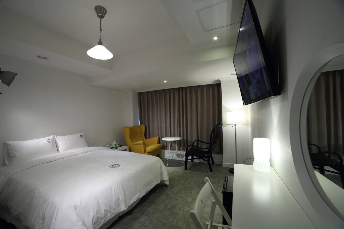 Ein Hotelzimmer mit einem großen Bett, einem Flachbildfernseher, einem Schreibtisch mit Lampe und einem Sessel.