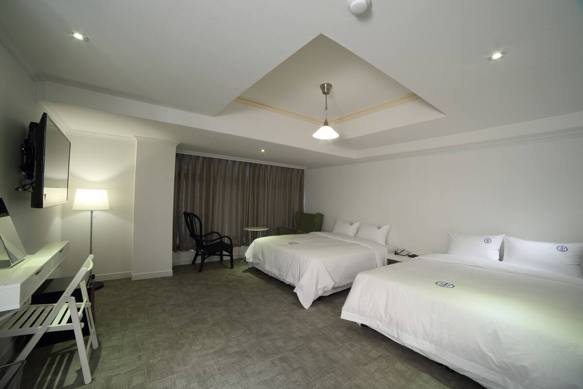 Ein Hotelzimmer mit zwei Betten, einem Schreibtisch, einem Stuhl, einem Fernseher und einer Deckenleuchte.