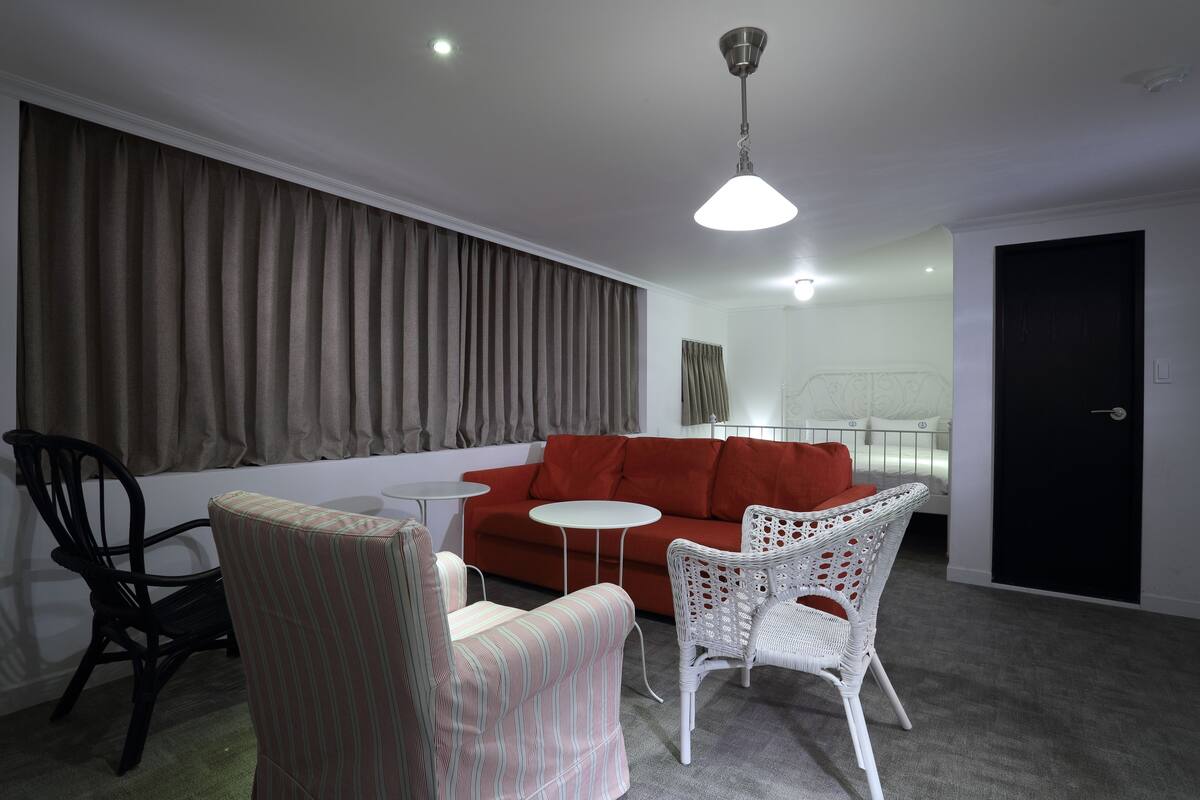 Ein modernes Wohnzimmer mit einem roten Sofa, weißen Korbstühlen, einem kleinen runden Tisch und einem schwarzen Sessel.