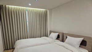 Hotellihuone, jossa on kaksi sänkyä, puinen pääty ja suuri ikkuna, jossa on verhot.
