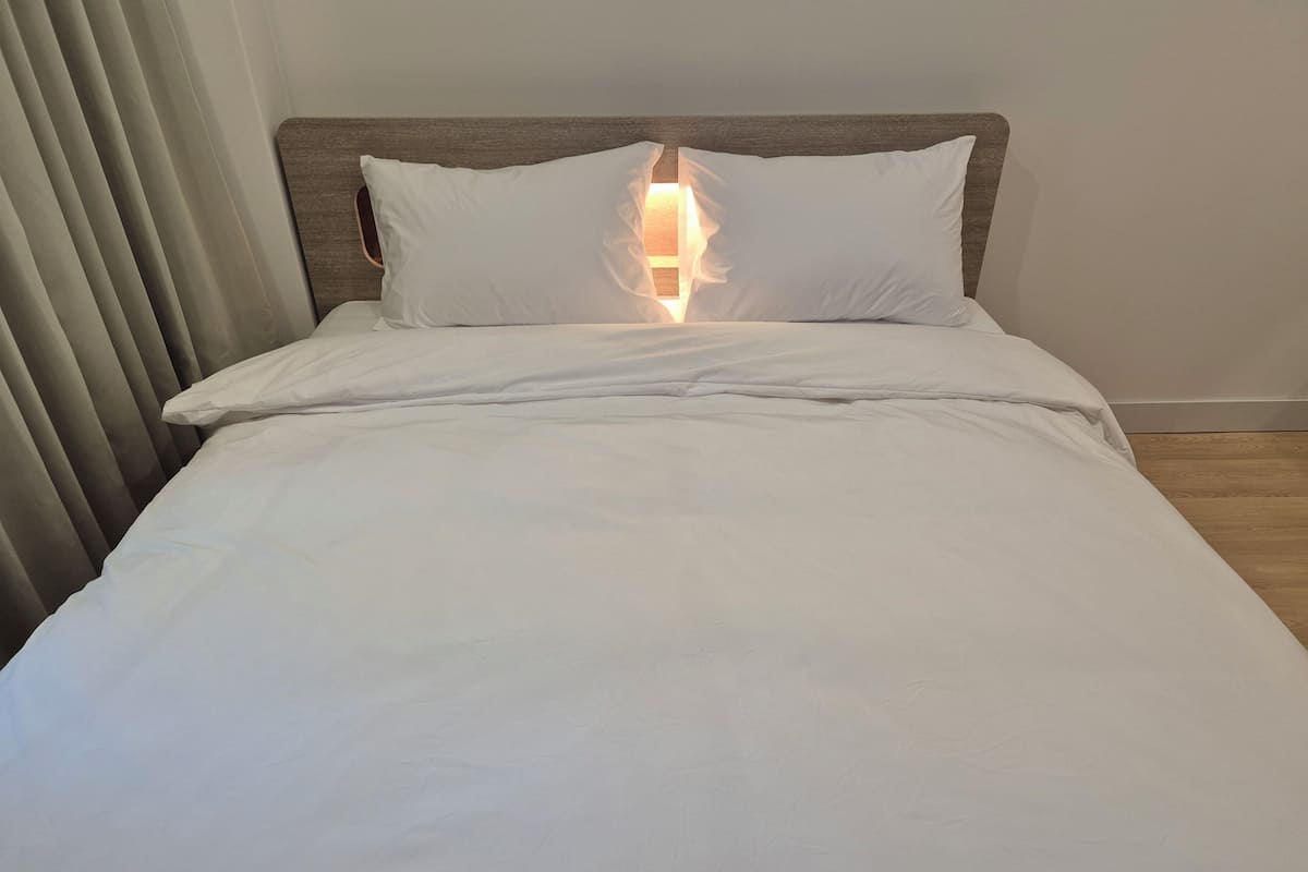 A neatly made bed with white linens and a wooden headboard.