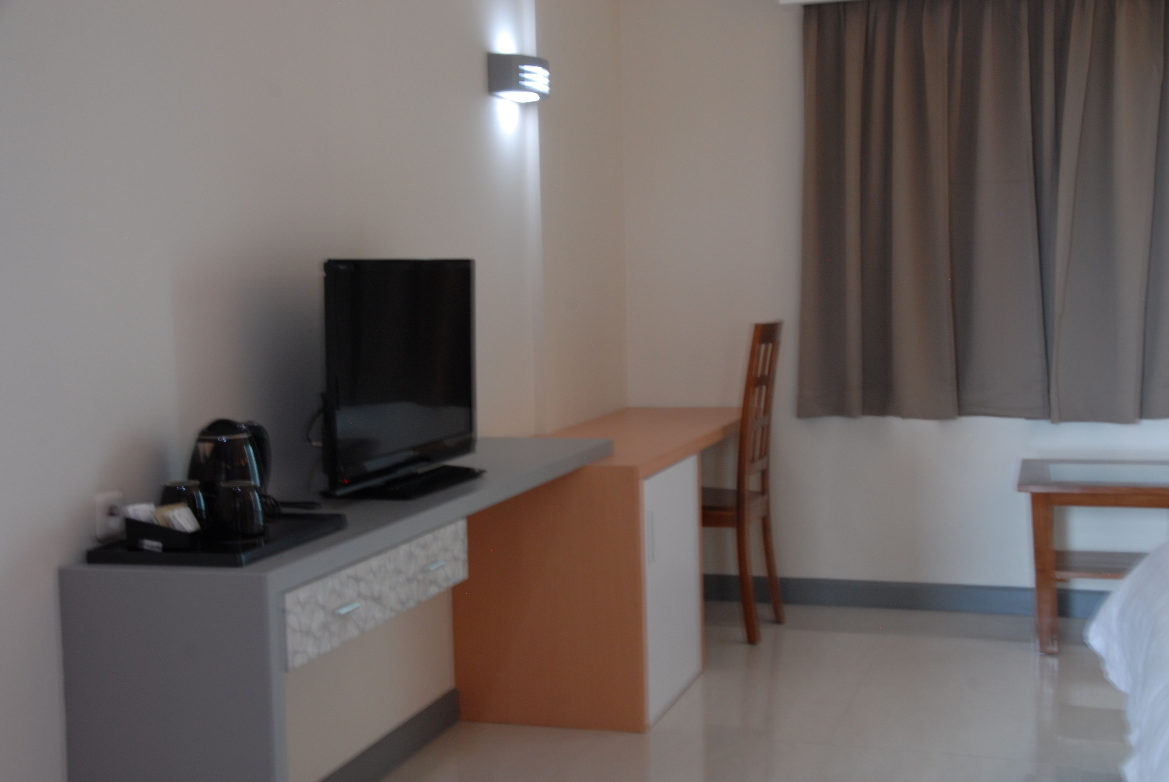 Una habitación de hotel moderna con una televisión de pantalla plana sobre un mueble empotrado, una cafetera, una silla de madera y una mesita pequeña.