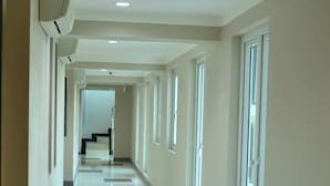 Un largo pasillo bien iluminado con suelo de baldosas, ventanas amplias y una unidad de aire acondicionado instalada en el techo.