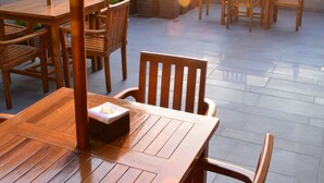Un patio al aire libre con mesas y sillas de madera, plantas en macetas y sombrillas.
