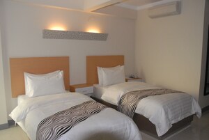 Habitación de hotel con dos camas, cada una con ropa de cama blanca y mantas de estampado de cebra. Se observa una unidad de aire acondicionado montada en la pared y una mesita con un teléfono encima.