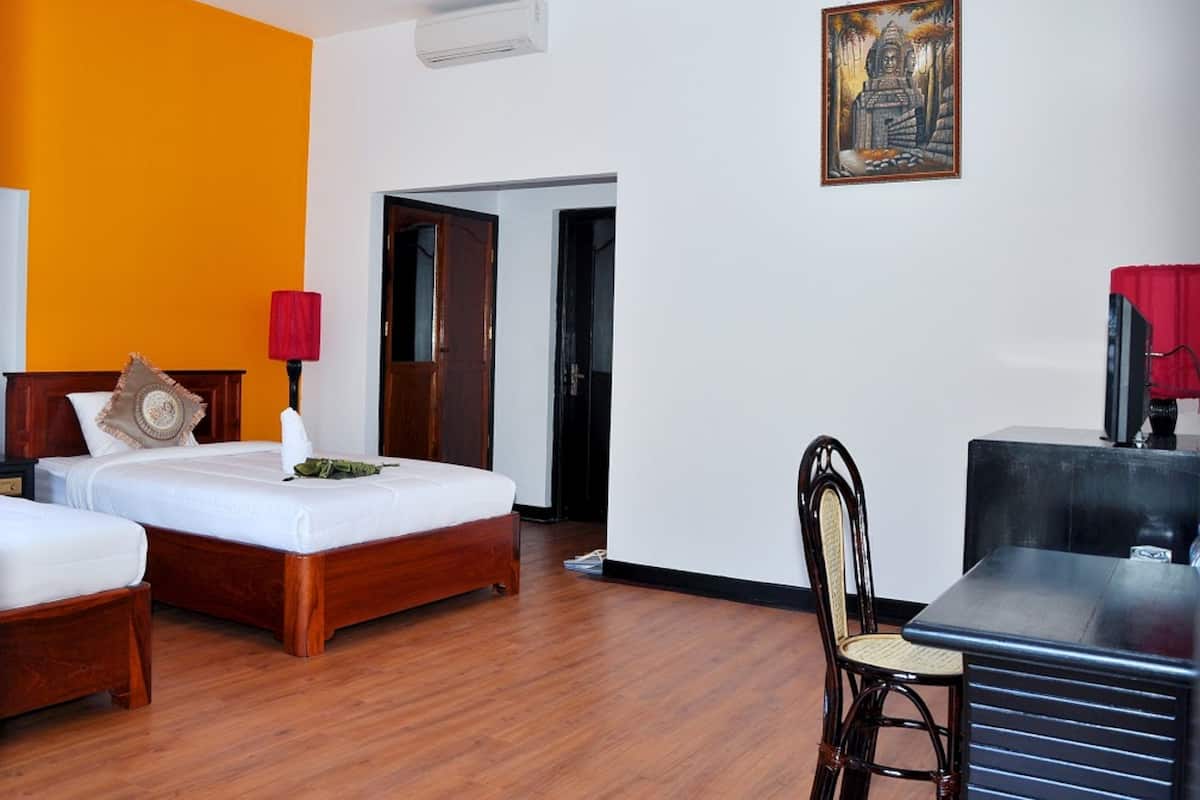 Habitación de hotel con dos camas de madera, un escritorio con silla, una lámpara roja y un cuadro en la pared.