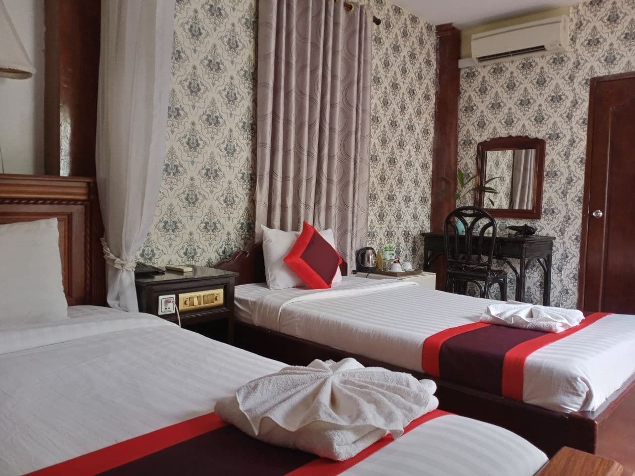 A hotel room with two beds, a nightstand, a chair, and a mirror.