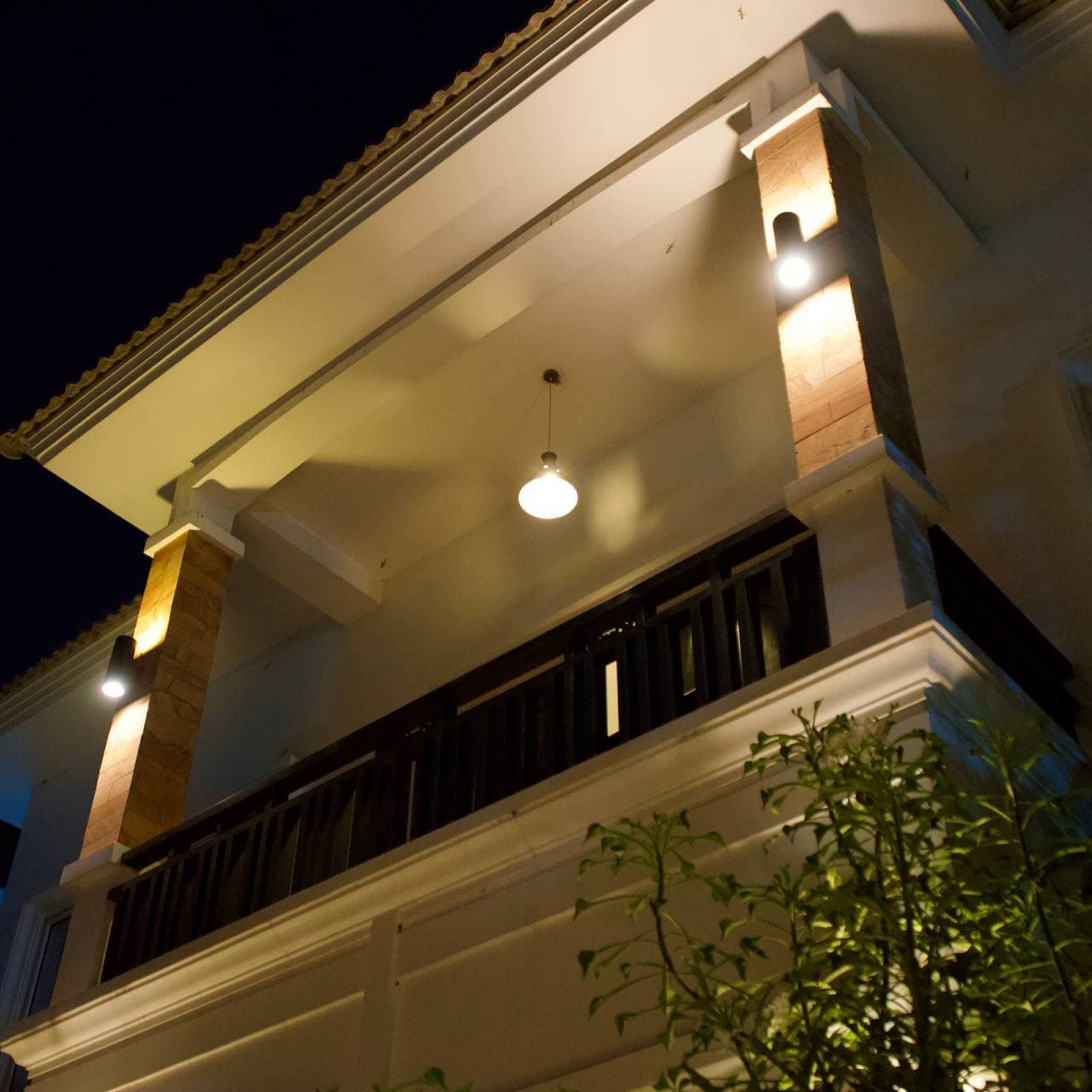 A building with a balcony, a light fixture, and a plant in the foreground.