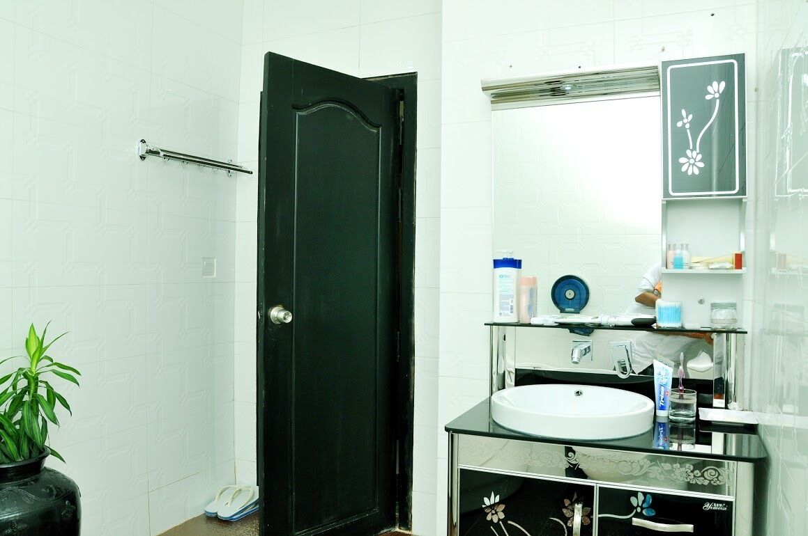 A bathroom with a black door, white tiled walls, a glass sink, and a mirror with a floral design.