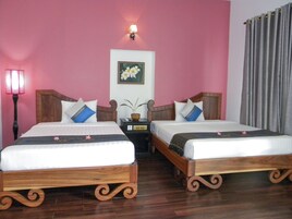 Una habitación de hotel con dos camas de madera, una mesita de noche con lámpara, una luz en la pared y un cuadro enmarcado.