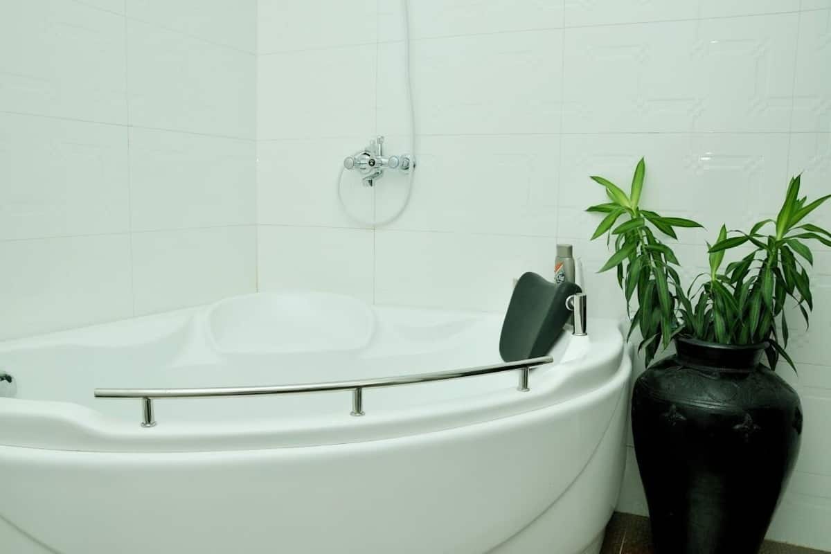 Una bañera blanca con ducha, un florero negro con plantas verdes y una pared de azulejos blancos.