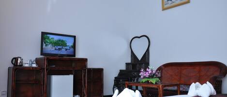 Habitación de hotel con televisión, una decoración con forma de corazón, sofá y cama con almohada decorativa.
