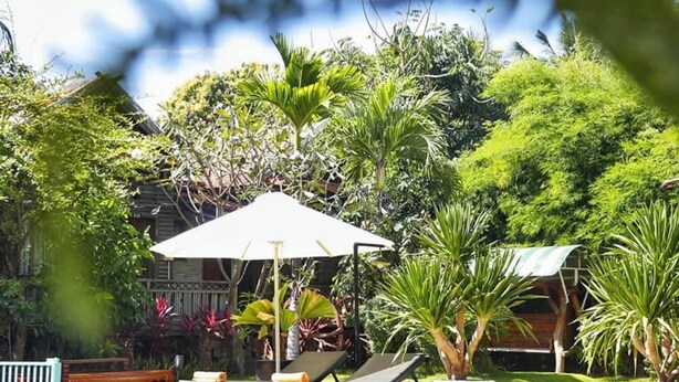 A swimming pool with lounge chairs and umbrellas, surrounded by lush greenery and a wooden fence. - Vimean Sovannaphoum Resort (Battambang)