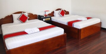 Dos camas de madera con ropa de cama blanca y detalles rojos, una mesita de noche con lámpara, y un enchufe.