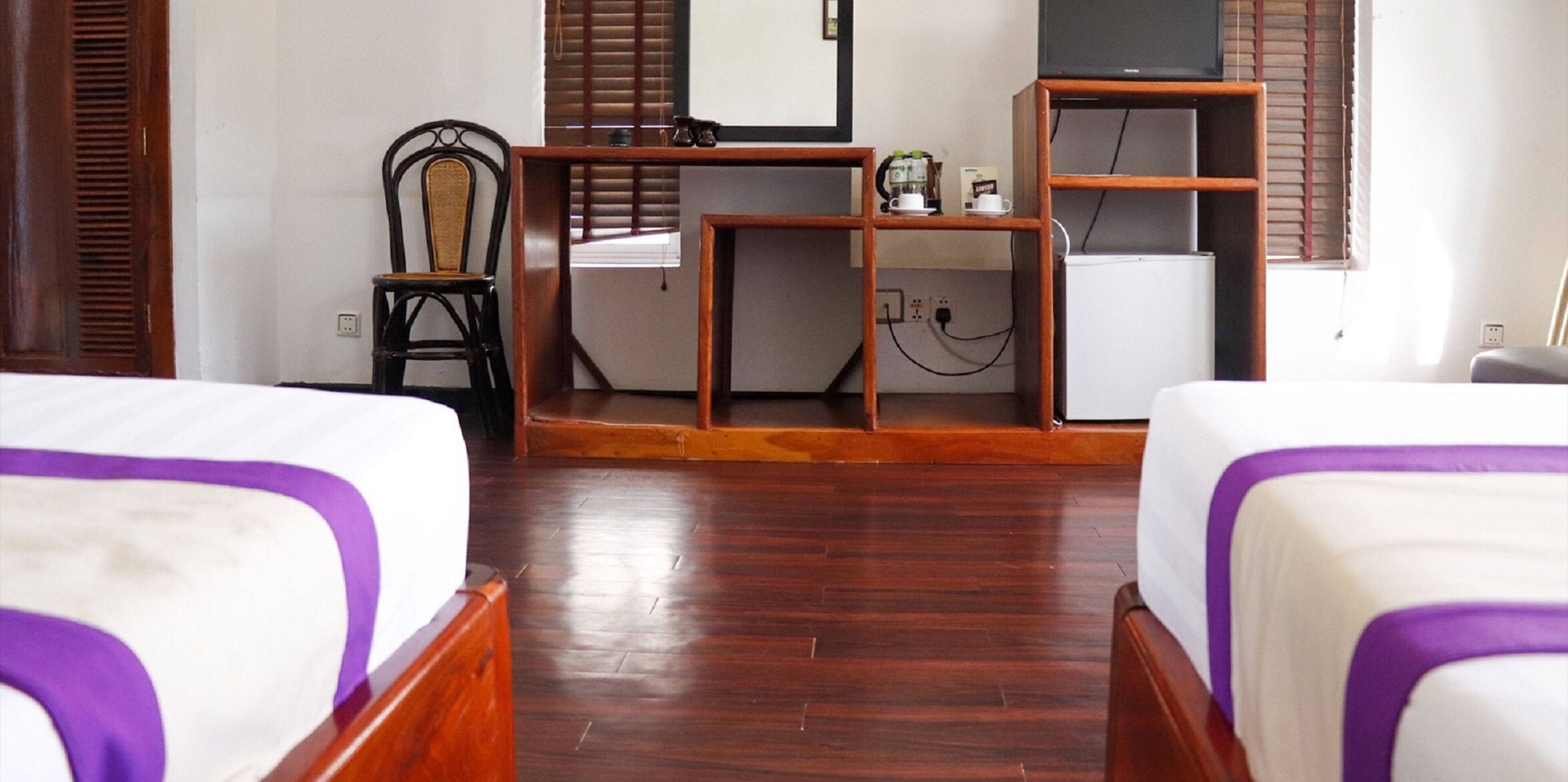 Habitación de hotel con dos camas, un escritorio, una silla, un televisor y un refrigerador pequeño.